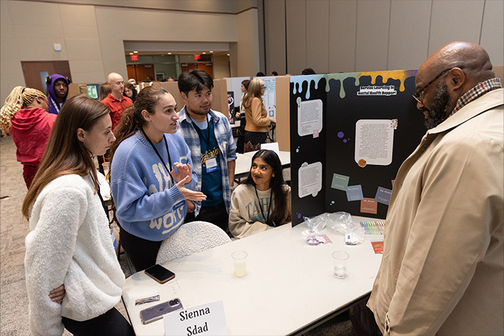 A group of students in the Campus Center event room discuss a poster presentation