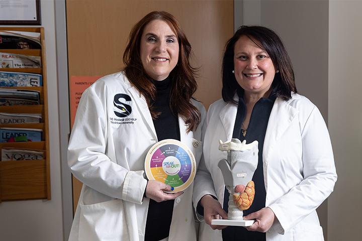 Two Stockton faculty members in white lab coats hold props that help them teach about language disorders
