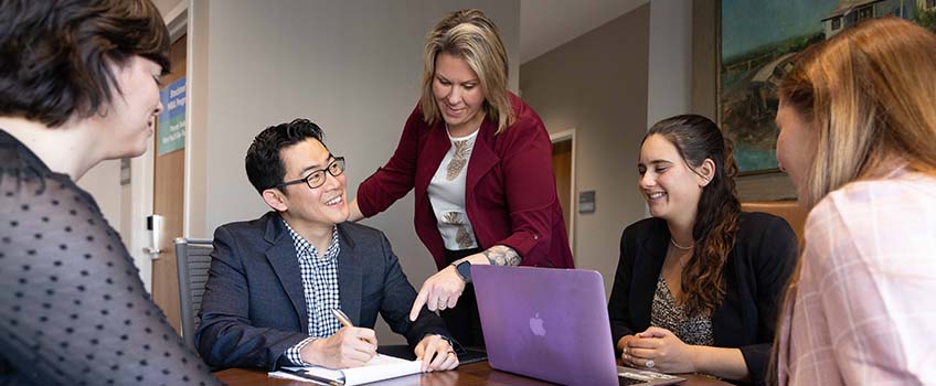 A business professor stands above a group of students collaborating at a table