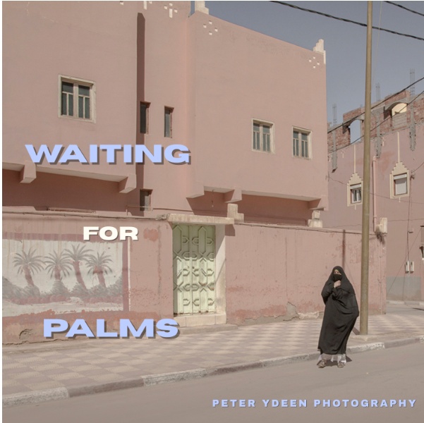 Peter Ydeen A photograph featuring a person in a black abaya and niqab standing on a sidewalk in front of a pink building, with the overlaid text "WAITING FOR PALMS" and "PETER YDEEN PHOTOGRAPHY."