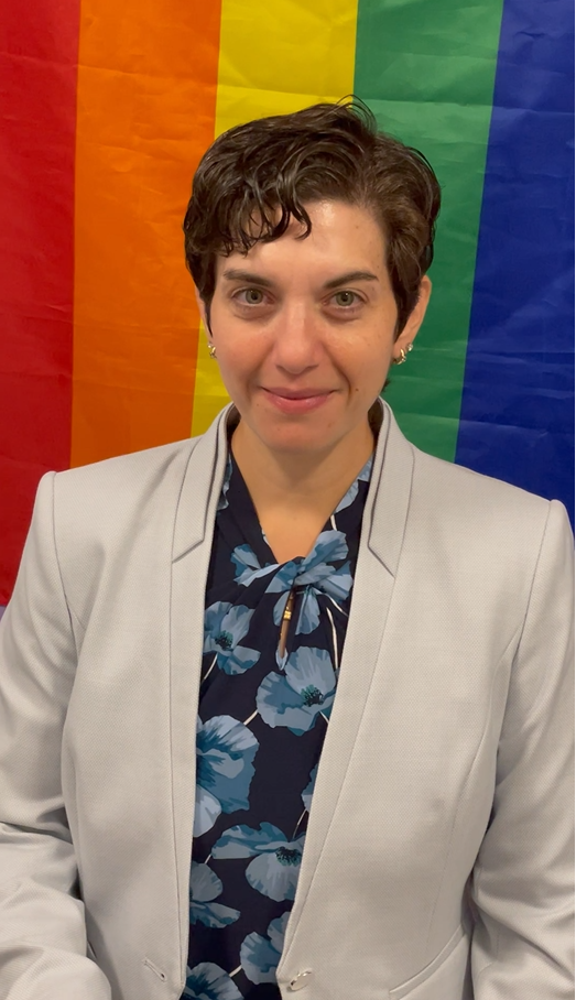 Dean of Students Haley Baum stands in front of a rainbow flag as she reflects on what LGBTQ+ History Month means to her.