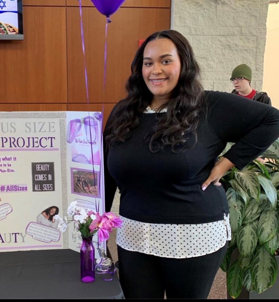 Senior Ahmiya Jones stand next to a poster explaining what The Plus-Size Project at Stockton University is
