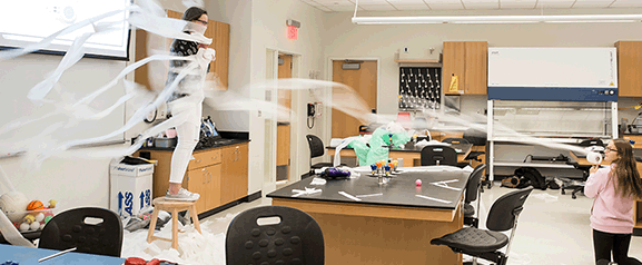 Girls send toilet paper flying in a workshop to demonstrate Bernoulli's Principle. Below students learn the science of brain scans and solder an electronic badge