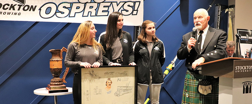 Members of the Stockton women's rowing team present Bob Garbutt with a poster made when he was coaching and signed by his former rowers