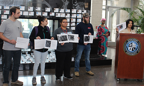 woman at podium and group of men and women students holding signs