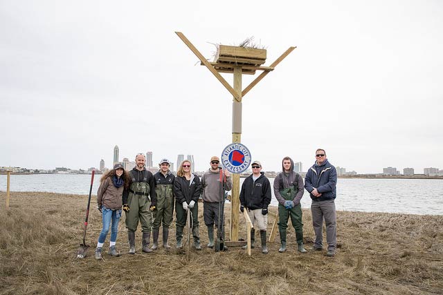 group of men and women standing in front of osprey platform nest 