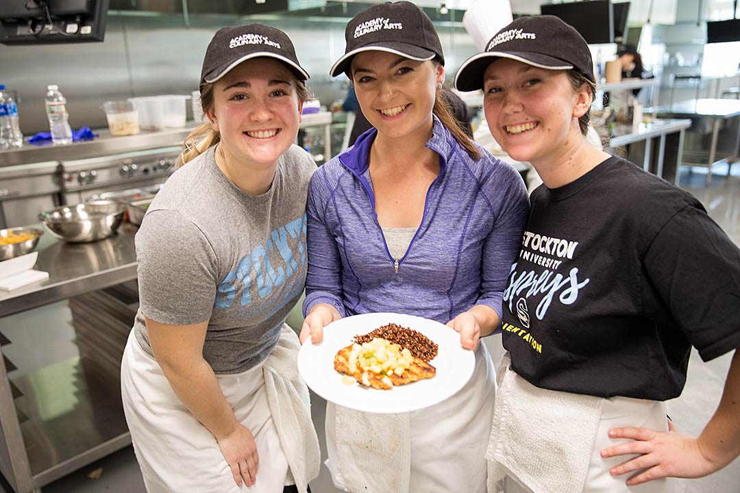 three female students smiling holding dish of food