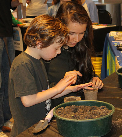 girl helping boy plant seed in pots
