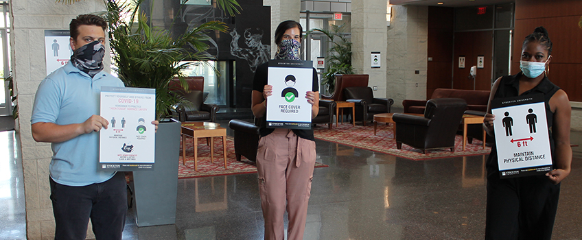 Signs with multiple messages are being posted around campus. Below, workers build some of the 600 hand sanitizing stations and campus partners are masked and ready.