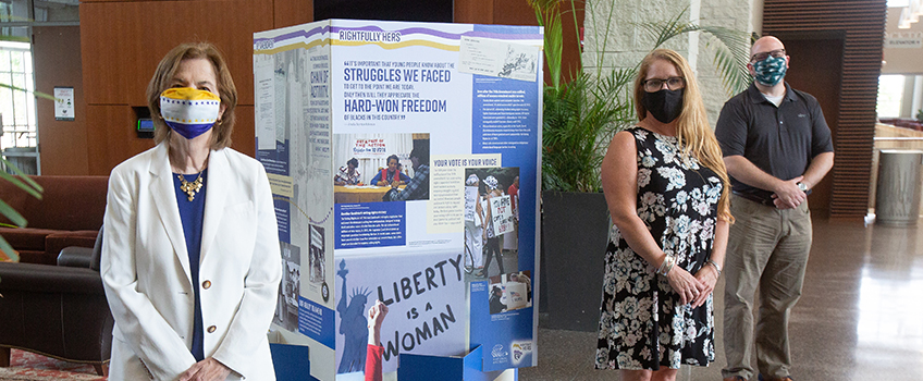 From left, Linda Wharton, wearing mask modeled after the suffragist flag, Sara Faurot, and Giancarlo Brugnolo with the pop-up “Rightfully Hers” exhibit on the 19th Amendment on display in the Galloway Campus Center lobby.