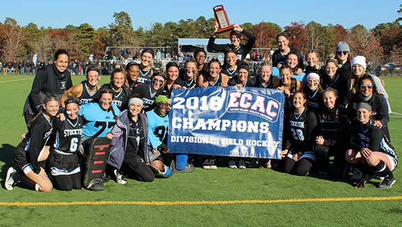 field hockey girls smiling outside around champion banner