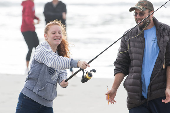 girl casting fishing rod on beach while man watches