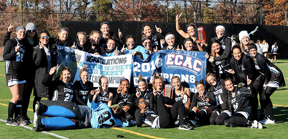 field hockey players smiling outside posing around banner 