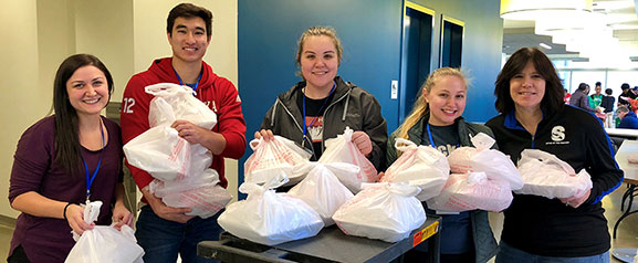 students and faculty member hold packaged meals