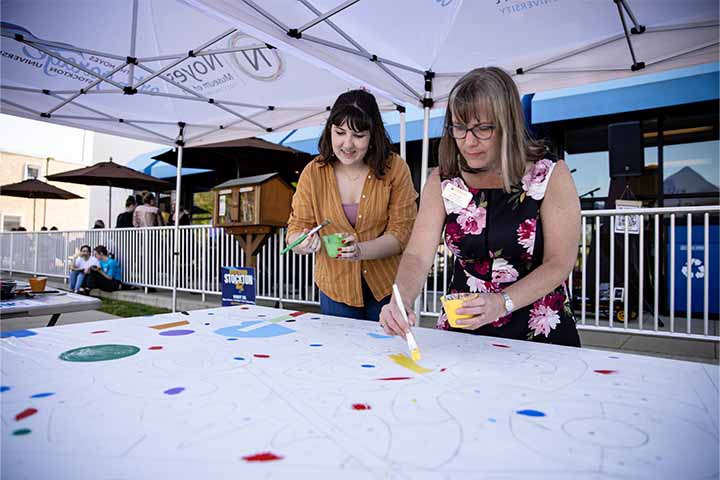 Two women add paint to a large white canvas
