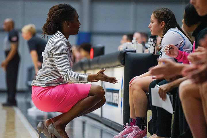 Devin Jefferson in pink skirt kneels in front of basketball player sitting in chair on sideline