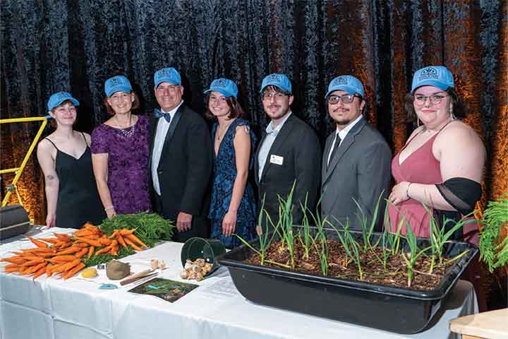 Students and Bil Leipold with blue Stockton caps with produce grown on the Sustainability farm