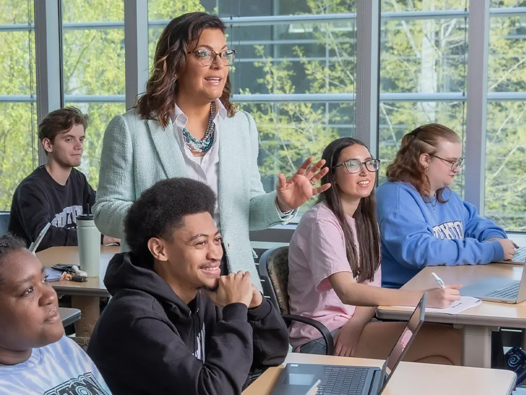 Stockton University professor engaging with students in a classroom, with students listening and working on laptops.