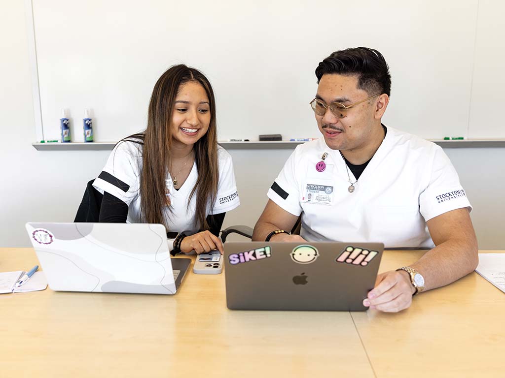 Two Stockton University nursing students sitting at a table and looking at their laptops