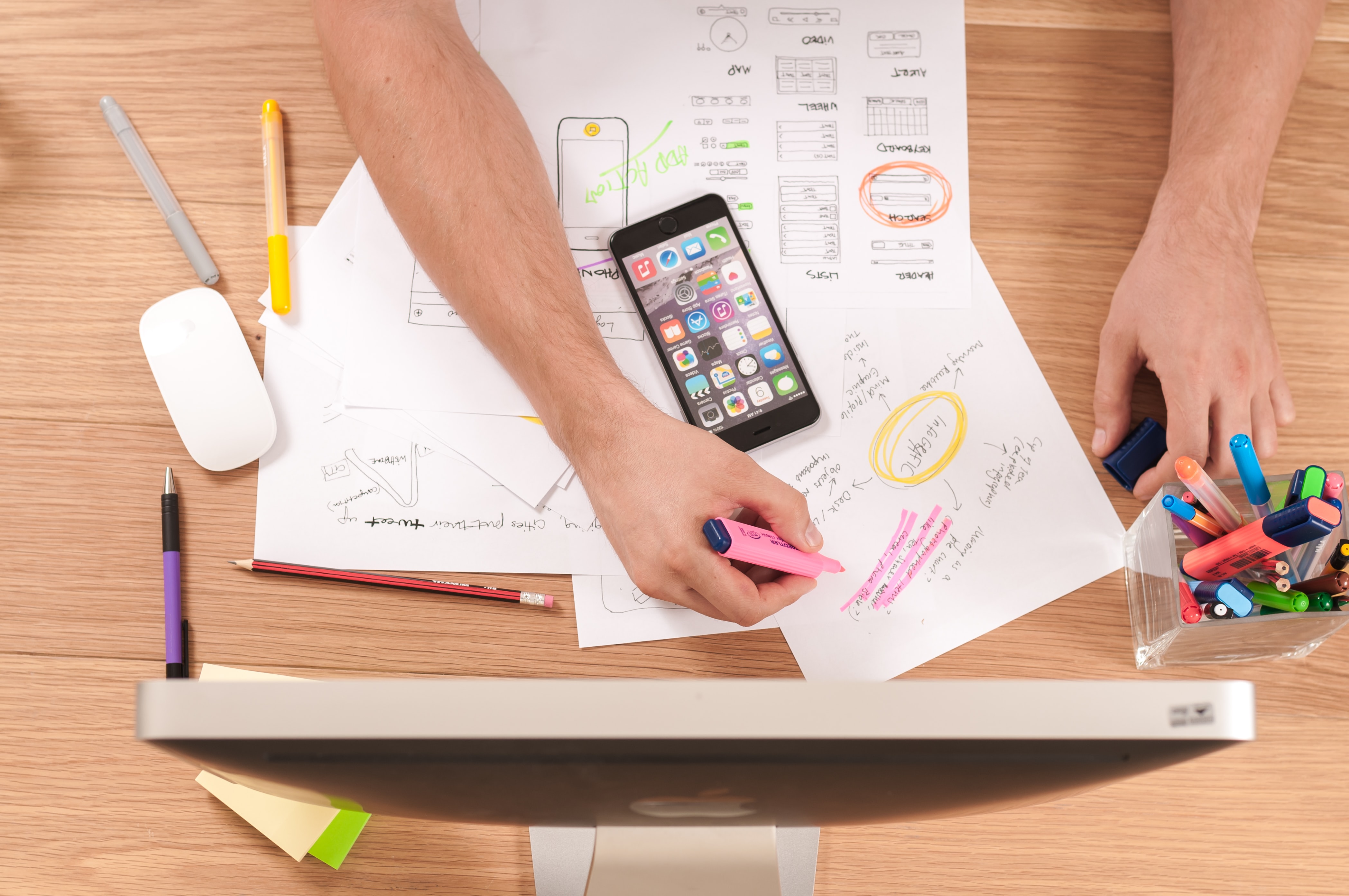 person writing on white paper with pink highlighter, phone is on top of white paper